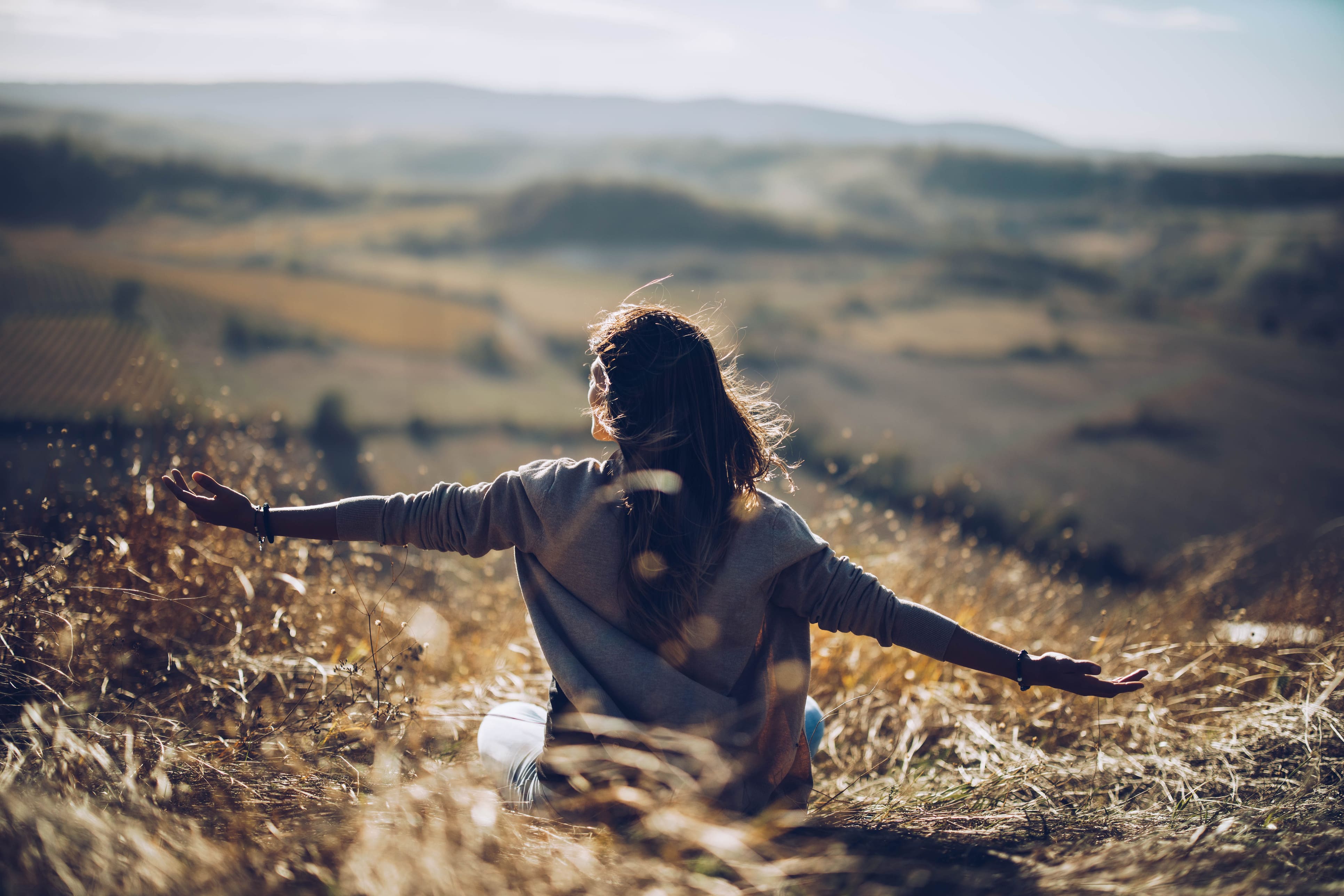 Une femme dans un champ ensoleillé, les bras ouverts, profitant d'un moment de sérénité en pleine nature